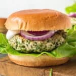 square image of a greek turkey burger with tzatziki sauce, sliced red onion, and lettuce