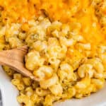 square image of a wooden spoon stuck into a dish of green chile mac n cheese