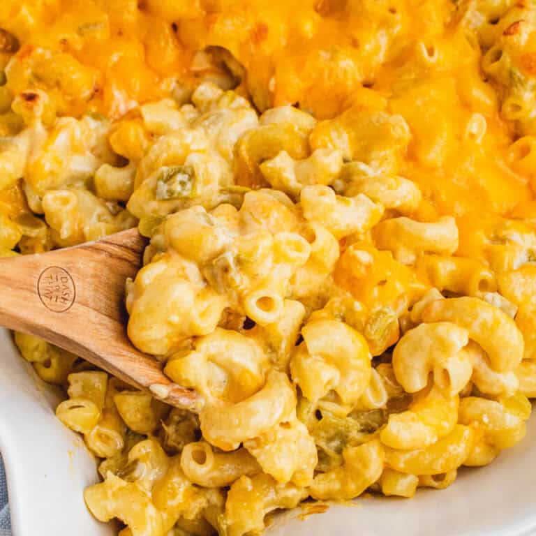 square image of a wooden spoon stuck into a dish of green chile mac n cheese