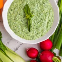 bowl of green goddess dip topped with basil and surrounded by veggies with recipe name at the bottom