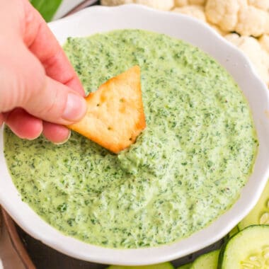 square image of a hand dipping a cracker into a bowl of green goddess dip