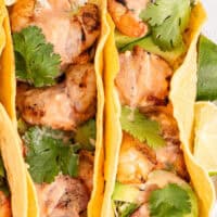image of of bacon wrapped shrimp tacos on a plate with lime wedges with the title the post on top with pink and black lettering