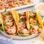 square image of bacon wrapped shrimp tacos on a plate with lime wedges