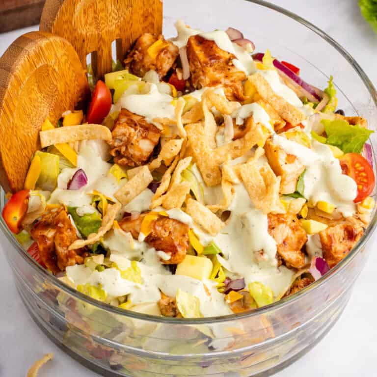 square image of grilled barbecue chicken salad in a glass bowl with wooden salad servers