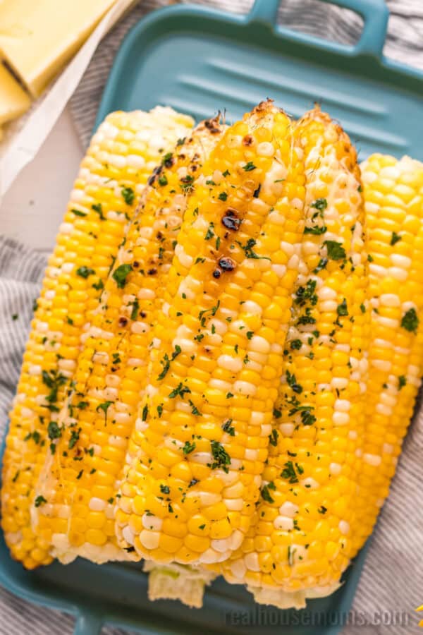 stacked ears of grilled corn on the cob next to pats of butter