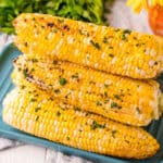 square image of grilled corn on the cob with butter and seasoning stacked on a platter