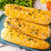square image of grilled corn on the cob with butter and seasoning stacked on a platter