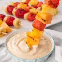 square image of a grilled fruit kabob being dipped into brown sugar dip