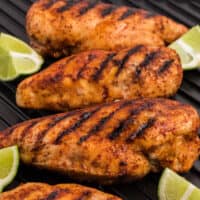 square image of honey lime chicken breasts on a grill pan with lime wedges