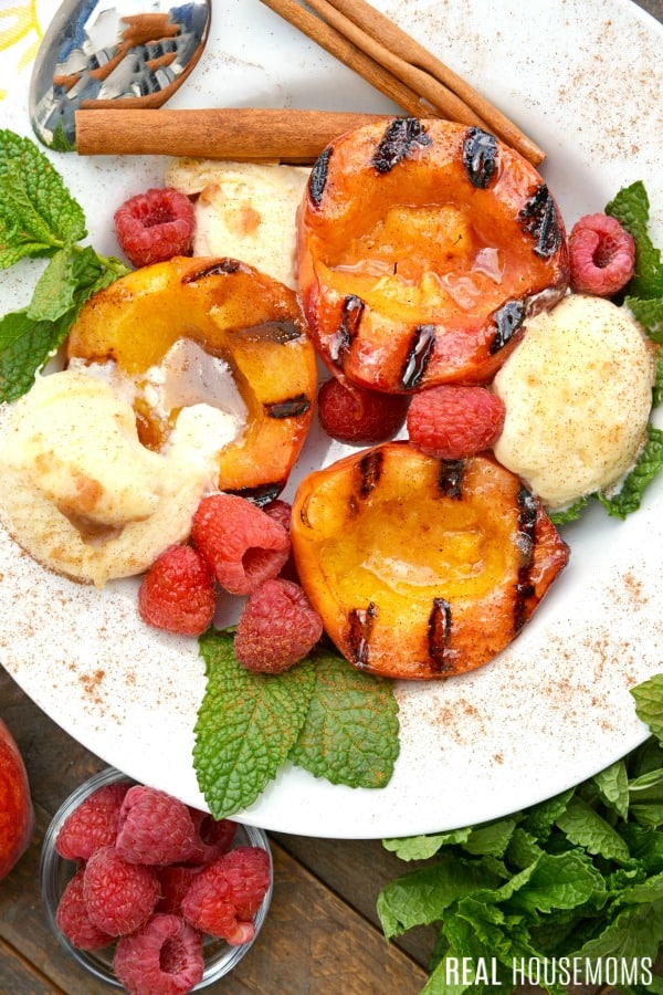 grilled peaches in a bowl with vanilla ice cream, raspberries, and mint