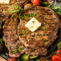 square image of a grilled ribeye steaks topped with butter, herbs, and finishing salt