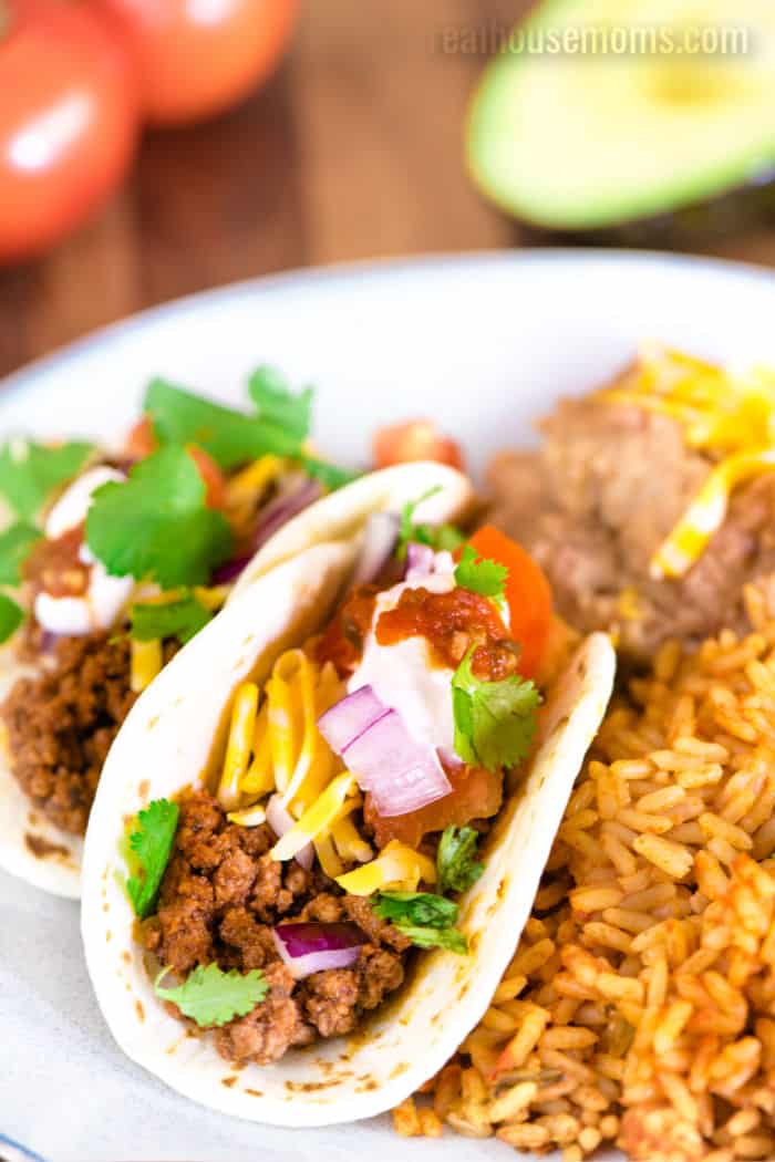 ground beef tacos on a plate with mexican rice and refried beans