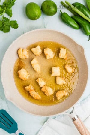 coated halibut pieces being fried in oil in a skillet