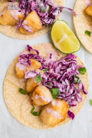 pan fried halibut pieces and cilantro lime coleslaw on a corn tortilla next to a lime wedge
