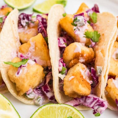 square image of halibut tacos on a plate with lime wedges