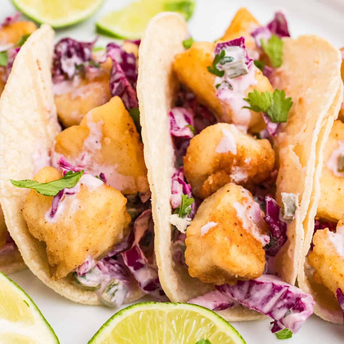square image of halibut tacos on a plate with lime wedges