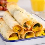 square image of ham & egg breakfast taquitos piled on a serving platter