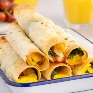 square image of ham & egg breakfast taquitos piled on a serving platter