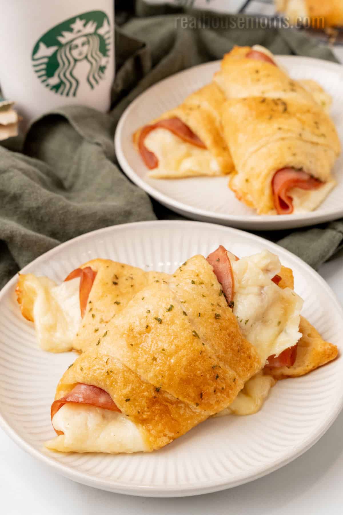 two copycat starbucks ham and swiss croissants on a small plate next to a starbucks coffee cup