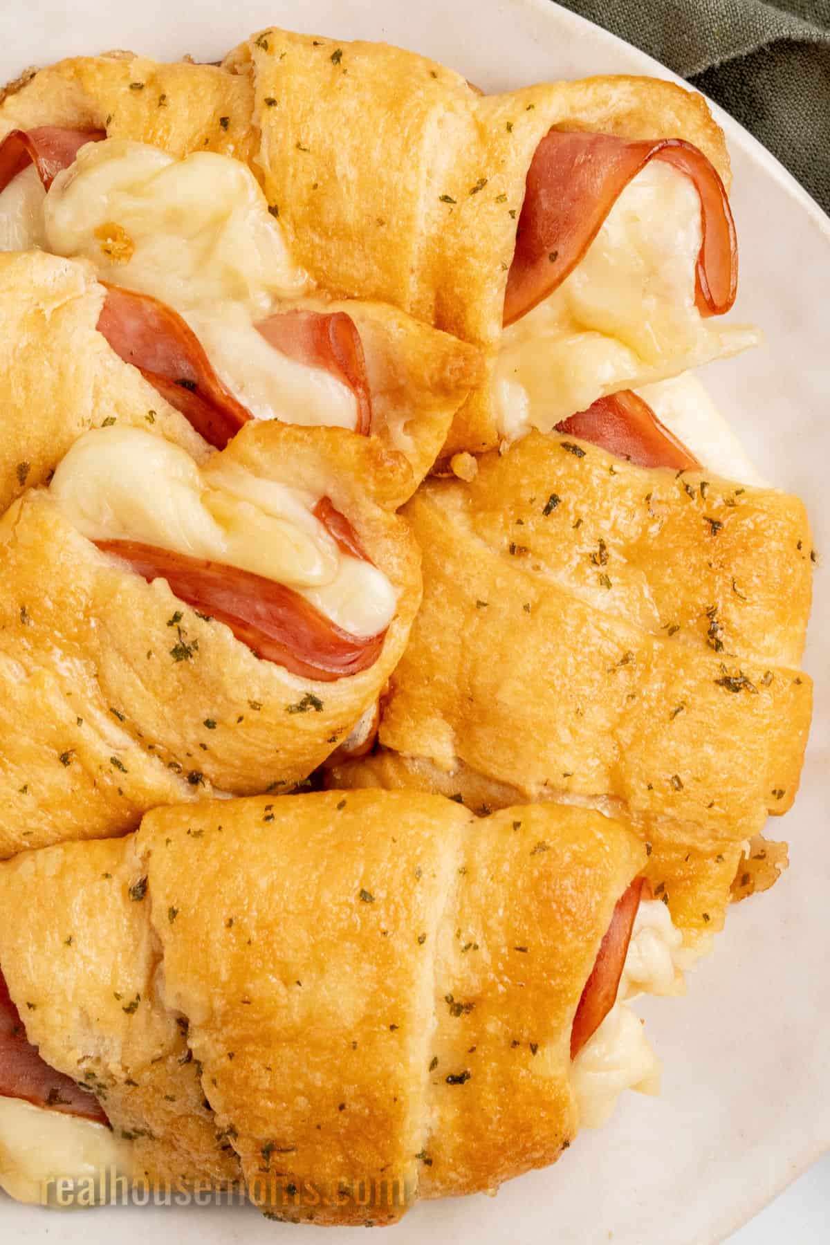 close up of ham and cheese crescent rolls piled on a white plate