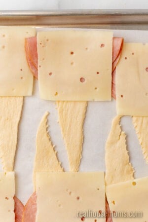 ham and swiss cheese slices on a crescent roll triangle on a lined backing sheet