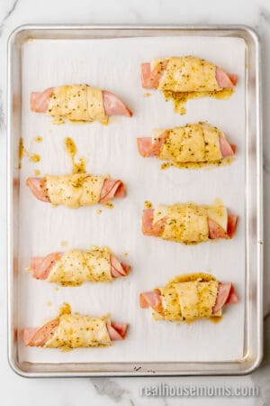 ham and cheese crescent rolls brushed with glaze on a lined baking sheet