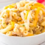 square close up image of hamburger mac and cheese in a bowl with shredded cheese on top