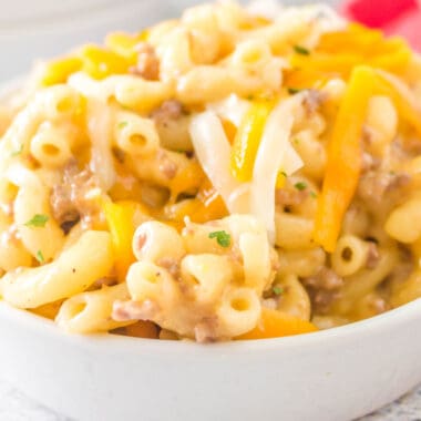 square close up image of hamburger mac and cheese in a bowl with shredded cheese on top