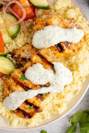 harissa chicken topped with yogurt sauce over couscous