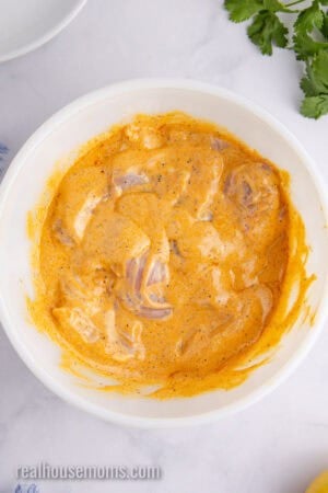 large bowl of boneless skinless chicken thighs coated in harissa marinade