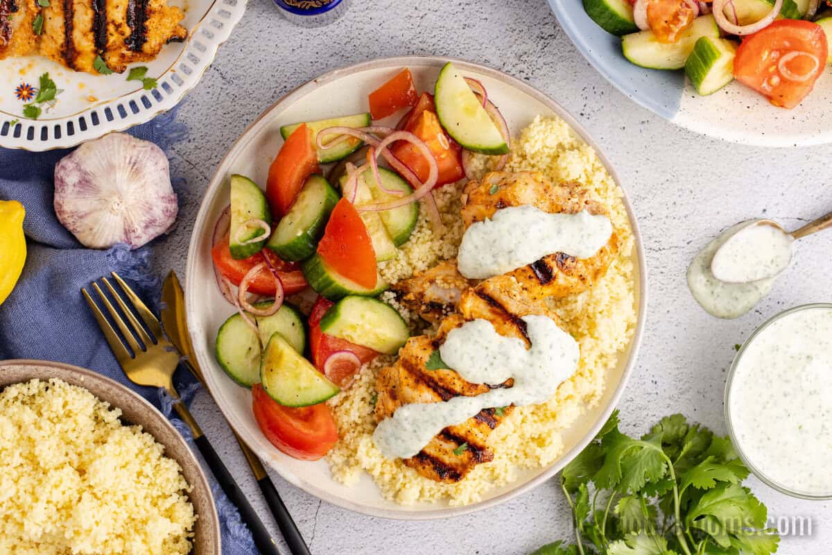 harissa chicken with yogurt sauce served over couscous with cucumber tomato salad