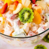 close up of hawaiian cheesecake salad in a glass bowl with fruits on top of the salad and recipe name at the bottom