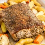 square image of a herb crusted pork loin on a baking sheet with roasted vegetables