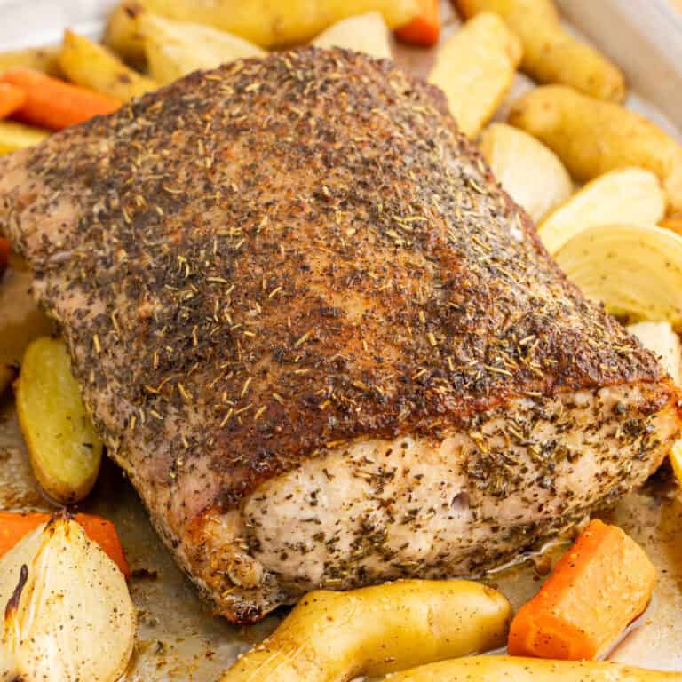 square image of a herb crusted pork loin on a baking sheet with roasted vegetables