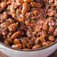 spoonful of homemade baked beans over the pot with recipe name at the bottom