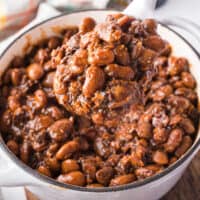 square close up image of homemade baked beans on a spoon over the pot