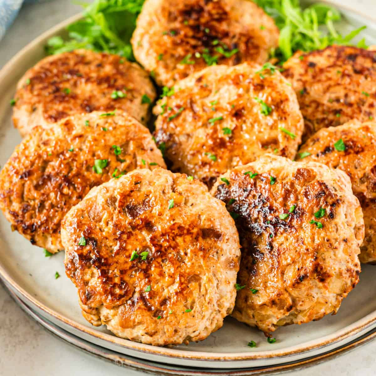 square image of homemade chicken apple sausage patties piled on a plate