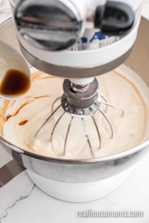 vanilla being poured into whipped heavy cream in a stand mixer bowl