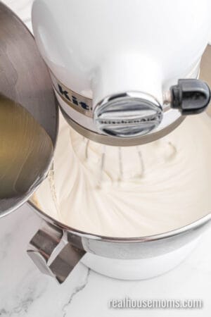 cooled gelatin mixture being poured into whipped cream in a stand mixer bowl