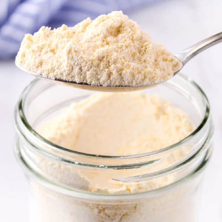 square image of homemade cornbread muffin mix on a spoon over the jar