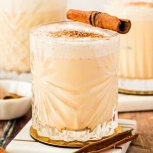 square image of a glass of homemade eggnog on a coaster with a cinnamon stick for garnish