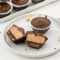 homemade peanut butter cups stacked up on a platter with one cut in half to show filling with recipe name at bottom