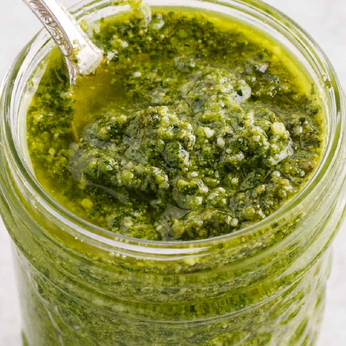 square close up image of homemade pesto sauce in a jar with a spoon