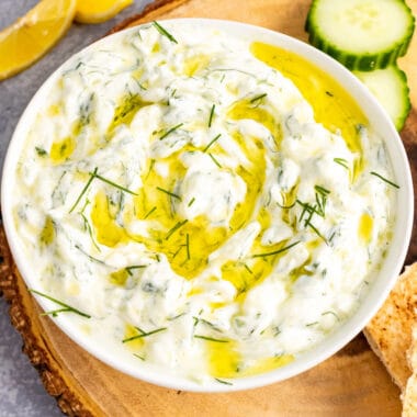 square image of homemade tzatziki sauce in a serving bowl topped with olive oil and dill