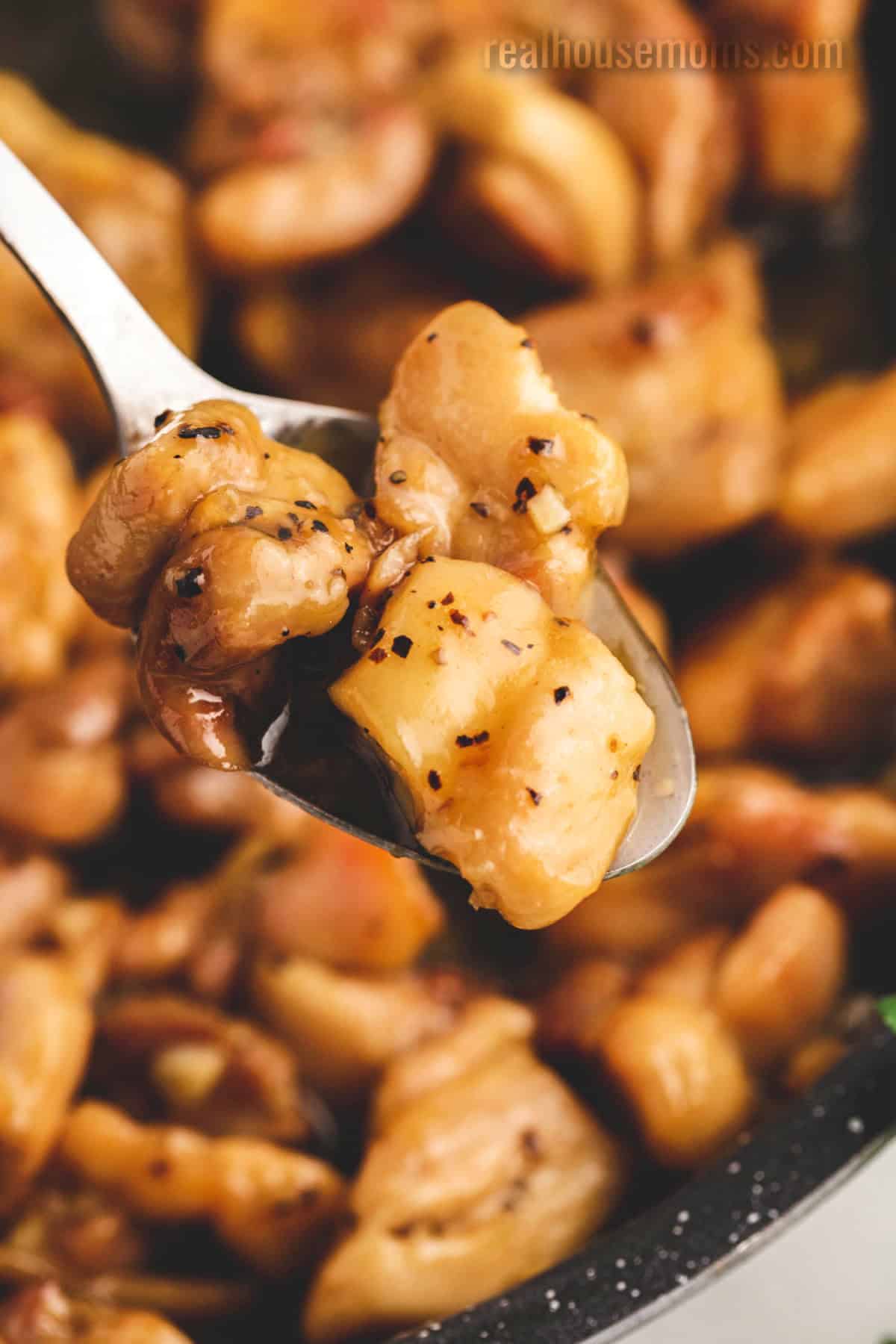 Honey Butter Chicken is better than take-out! If you want a quick and easy dinner then look no further than this juicy, sweet chicken dish! close up of honey butter chicken on a spoon over the skillet