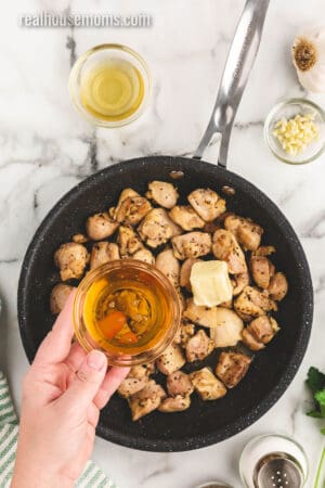 butter and honey being added to cooked chicken thigh chunks in a skillet