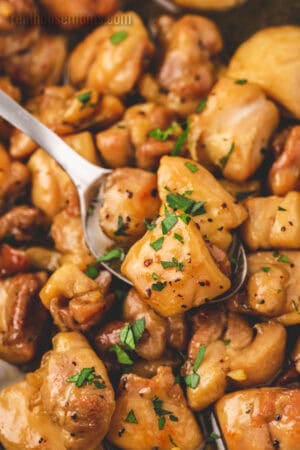 spoonful of honey butter chicken topped with chopped parsley over the skillet