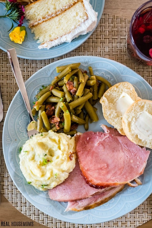 honey glazed crock pot ham slices on a plate with a roll, mashed potatoes, and green beans