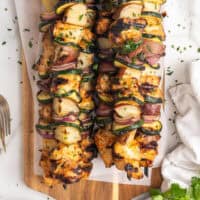 looking down at honey mustard chicken kabobs piled on a cutting board with recipe name at the bottom