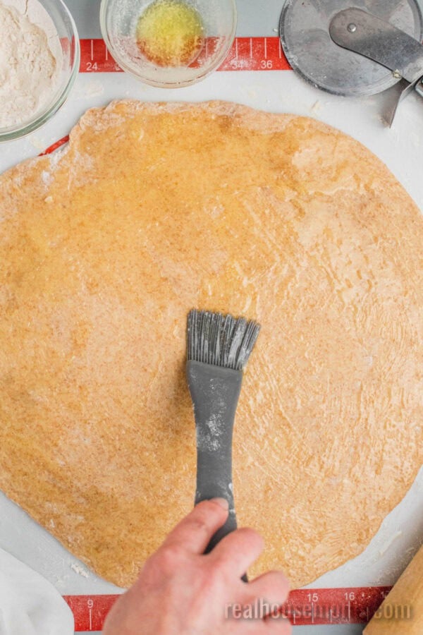 melted butter being brushed over honey wheat dough that's been rolled into a disc